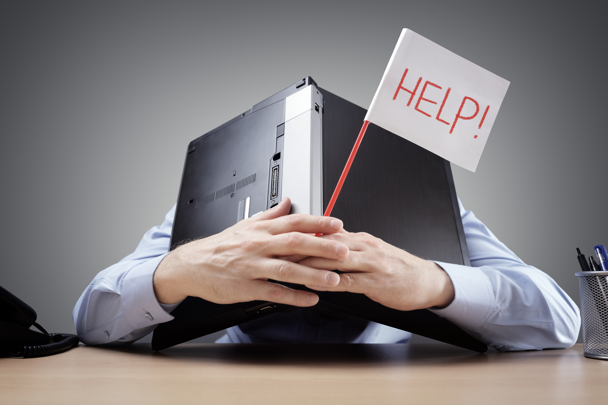 Salesperson suffering from burnout hiding behind his laptop and holding a flag with the word “help” written on it