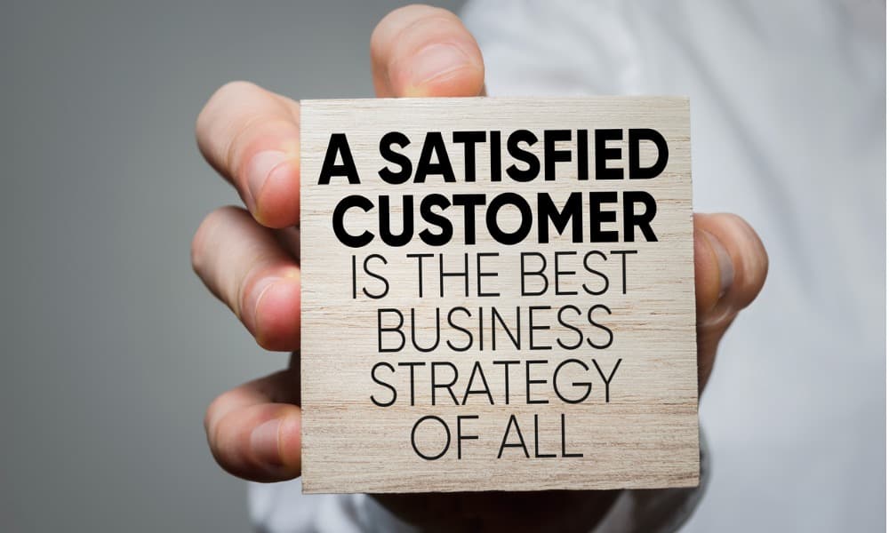 A hand holding a card that says, “A satisfied customer is the best business strategy.”