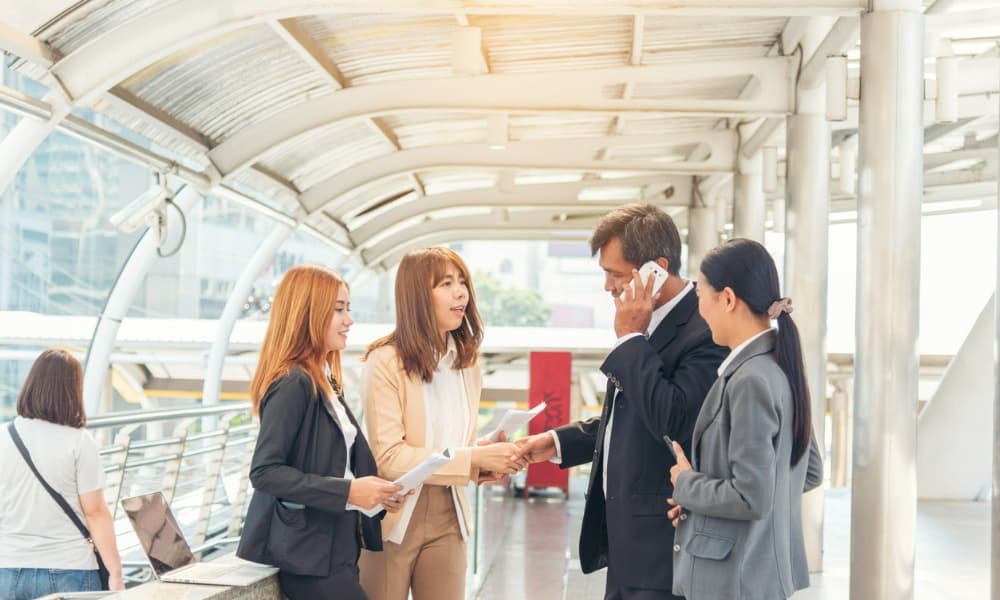 A salesman talking on his cell phone and shaking hands with a woman while her two associates look on.