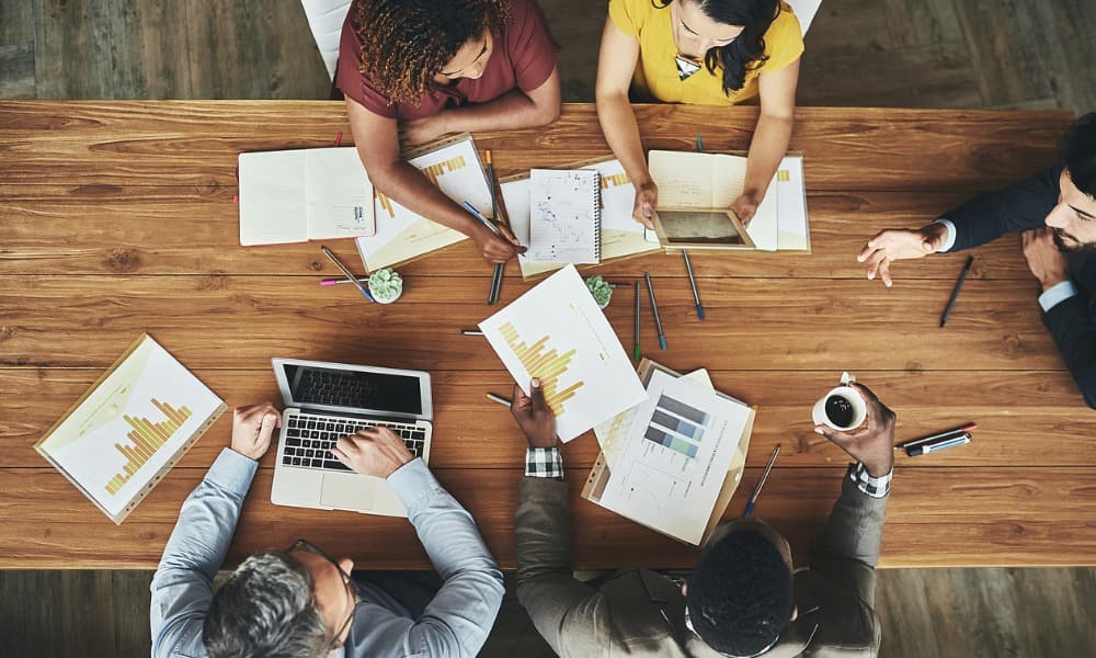 An overhead photograph of businesspeople sitting around a conference table looking at printouts of sales charts.