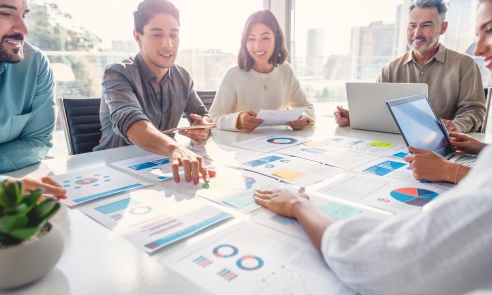 A group of people sitting around a conference table discussing an assortment of colorful sales charts.